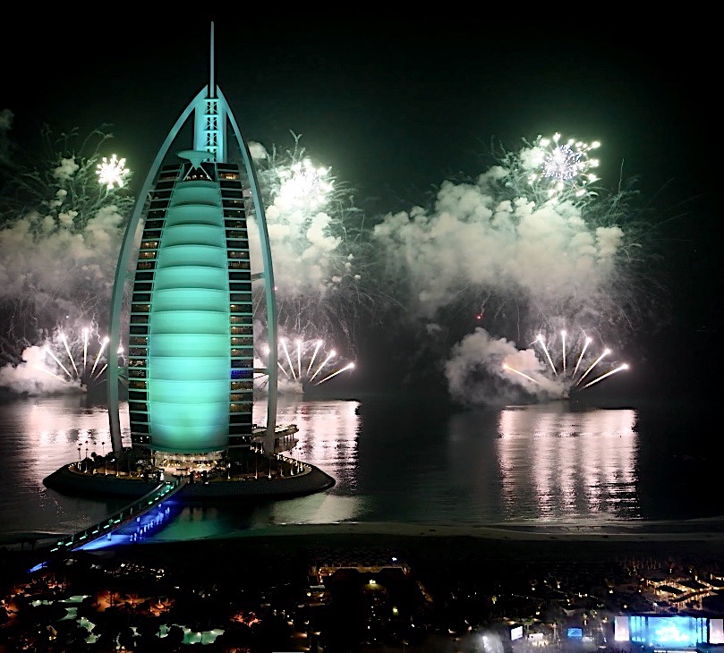 Fireworks over the sea behind the Burj Al Arab, lit green, filmed from above at night