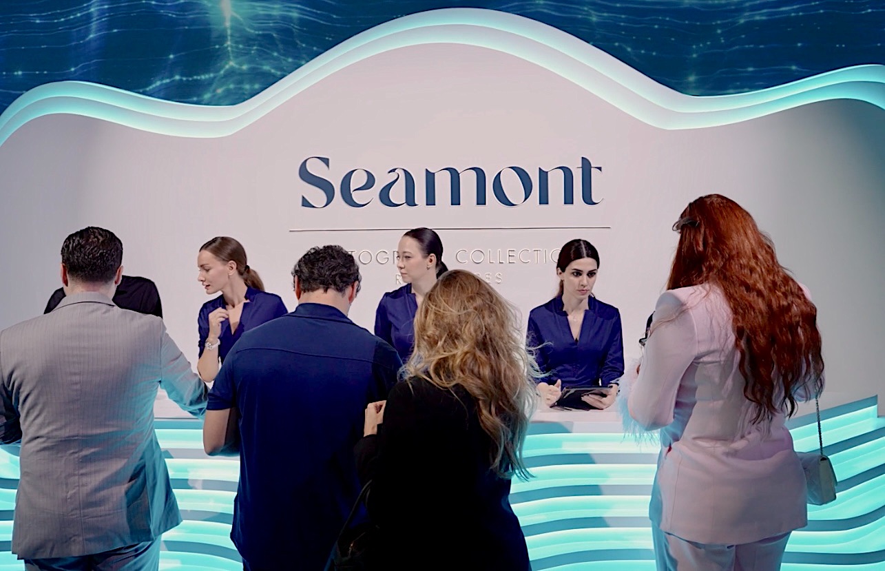 Guests checking in at a lit reception desk at a residences launch, hosts in navy behind the brand wall