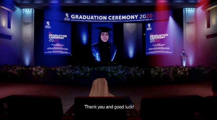 A virtual graduation ceremony 2020: a graduate on the big screen in a lit hall