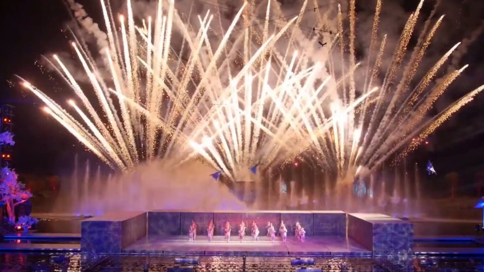 Fireworks bursting over the lake stage, the cast on the water