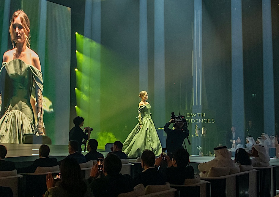 A model in a green gown on the runway at a residences launch, GAME camera operators filming from the floor