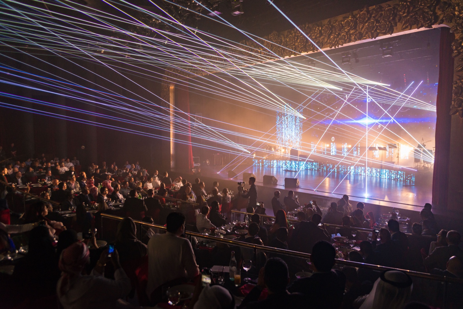 Laser show over a seated gala audience in a theatre, a camera operator filming from the floor